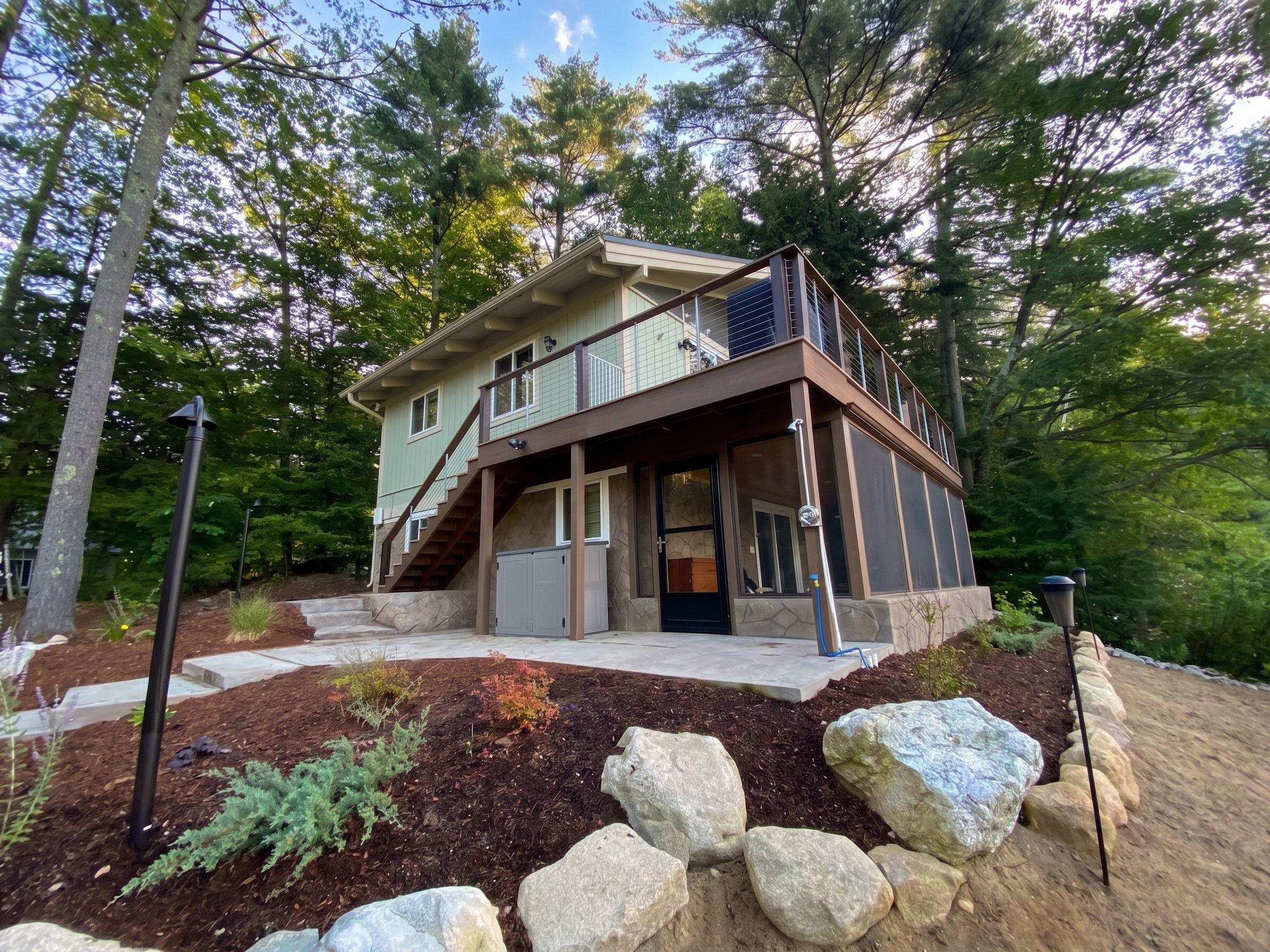A two-story house with a balcony, a stone facade, and a landscaped garden with rocks and shrubs.