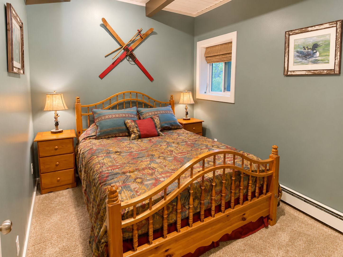 A bedroom with a wooden bed, two bedside tables with lamps, a window with a view, and a wall-mounted ski rack.