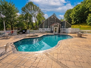 A swimming pool with a white fence, a lifeguard tower, and a building with a porch.