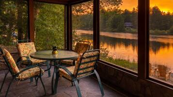 Un'area salotto esterna coperta con tavolo e sedie, con vista su un lago e alberi.