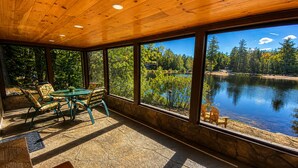 Ein Zimmer mit großem Fenster mit Seeblick, einem Tisch mit Stühlen und Steinboden.