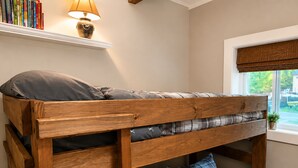 Ein Stockbett mit Holzbettrahmen, ein Nachttisch mit Lampe und ein Fenster mit Blick nach draußen.