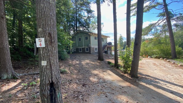 A forested area with a dirt path leading to a two-story building. - Pond-Side Chalet • Private Beach • Canoe & Kayak • Sleeps 7 • Near Storyland (Madison)