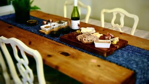 A wooden dining table with a blue table runner, white chairs, and a bottle of wine. - Pond-Side Chalet • Private Beach • Canoe & Kayak • Sleeps 7 • Near Storyland (Madison)