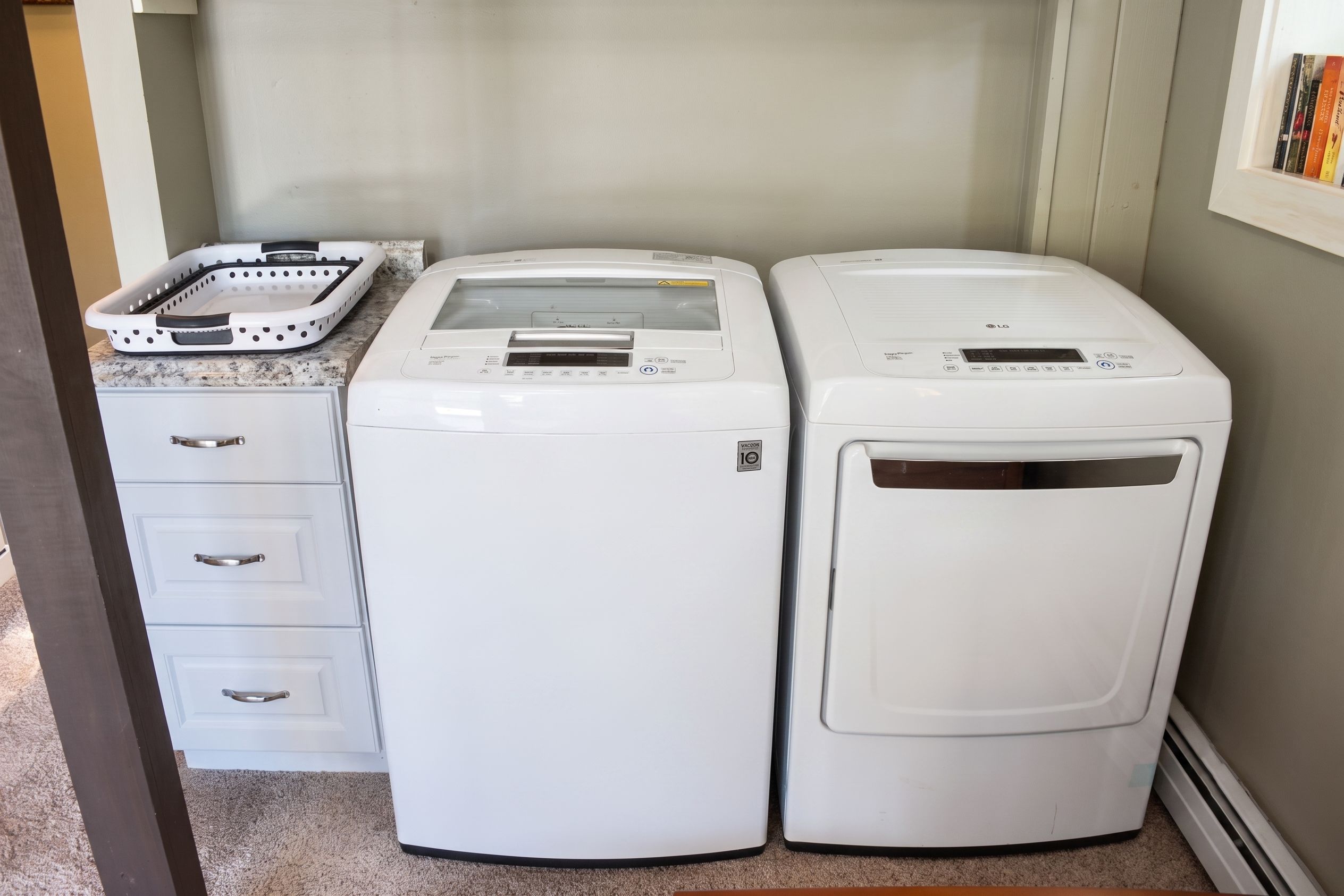A laundry area with two white washing machines, a white dryer, and a white laundry basket on a granite countertop.