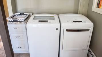 A laundry area with two white washing machines, a white dryer, and a white laundry basket on a granite countertop.