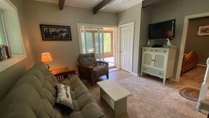 A living room with a sofa, armchair, coffee table, and a television on a cabinet. - Pond-Side Chalet • Private Beach • Canoe & Kayak • Sleeps 7 • Near Storyland (Madison)