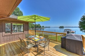 Une terrasse en bois avec une table et des chaises, un parasol vert et une vue sur un lac.