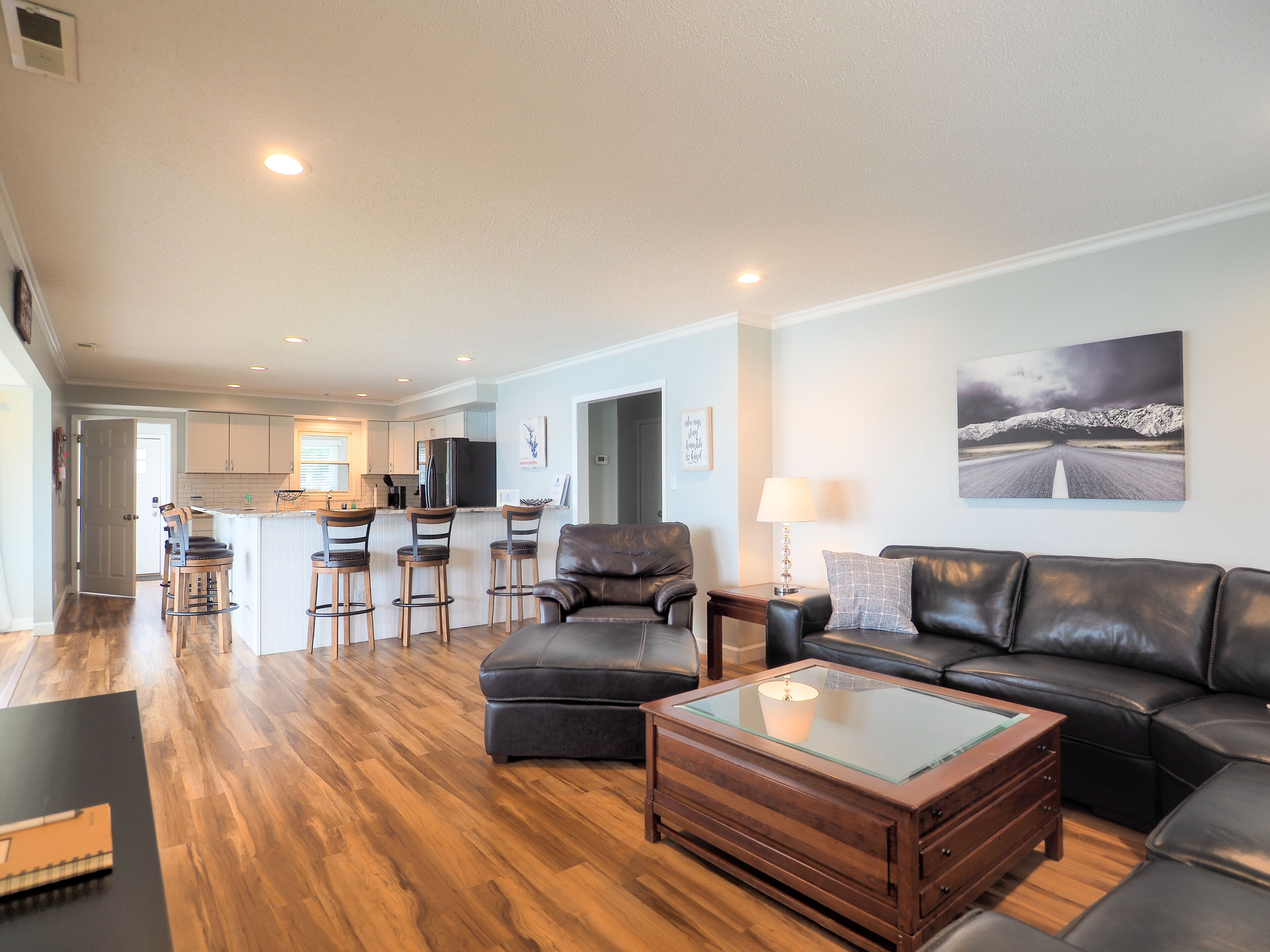 A modern living room with a leather sofa, a glass-top coffee table, and wooden flooring.