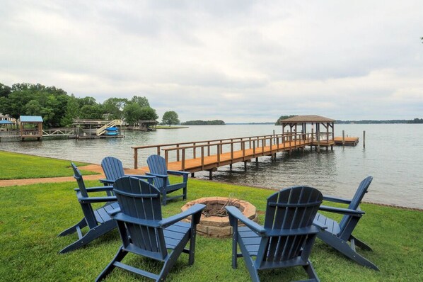 Une terrasse au bord du lac, avec des fauteuils Adirondack, un foyer et une jetée en bois qui s’avance dans l’eau.