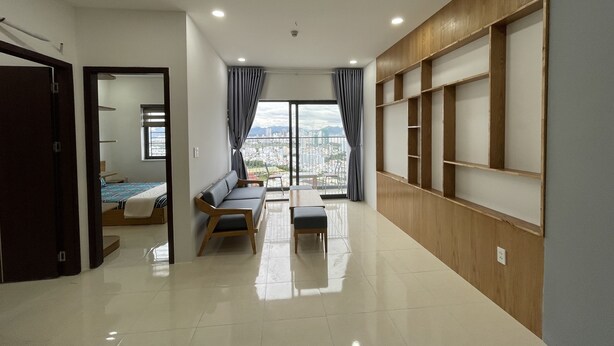 A modern apartment with a balcony, a sofa, a dining table, and a view of the cityscape. - Family Apartment with Seaview Balcony 03 (Nha Trang)