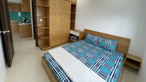 A bedroom with a large bed, wooden wardrobe, and a small bedside table. - Family Apartment with Seaview Balcony 03 (Nha Trang)