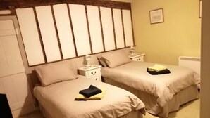 Une chambre avec deux lits simples, chacun doté d’une table de chevet et d’une lampe. La chambre est agrémentée d’une tête de lit en bois et d’un tableau encadré au mur.