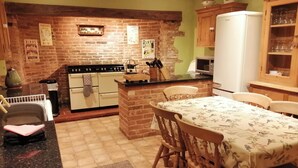 Une cuisine avec un mur en briques, un poêle, un réfrigérateur, des armoires en bois et une table à manger avec des chaises.