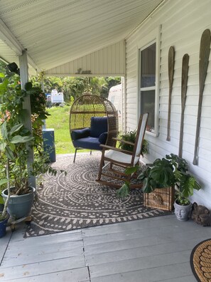 Une véranda abritée avec une chaise berçante, un fauteuil suspendu et des plantes en pot.