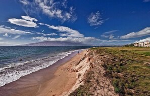 Een strand met een heldere lucht, golven en een berg in de verte.