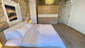Ein Schlafzimmer mit einem großen Bett, Steinwänden, Holzbalken, einer Hängeleuchte und einer Tür mit Klimaanlage.