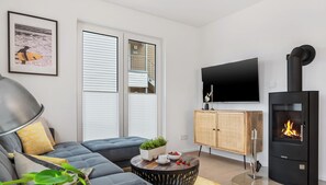 Una sala de estar moderna con un sofá seccional, una mesa redonda de centro, un televisor, una chimenea y un ventanal con persianas.