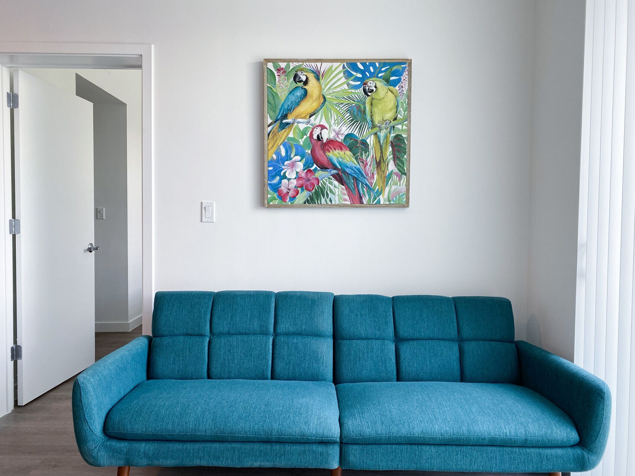 Un canapé de couleur turquoise dans une pièce dotée d’une porte et d’un tableau représentant des oiseaux et des fleurs, accroché au mur.