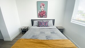 A bedroom with a bed, a nightstand, a bedside table, a window with blinds, and a painting on the wall. - Beautiful and spacious 2bed/2full bath apt (Miami)