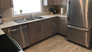 A modern kitchen with stainless steel appliances, wooden cabinets, and a window providing natural light. - Legal 2 bedroom suite conforms to the new 2024 Short Term Rental Regulations.  (Oliver)