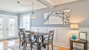 Een eethoek met een tafel, stoelen, een hanglamp, een lijst met een afbeelding aan de muur, en een bijzettafeltje met een lamp en een vaas.