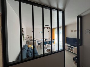 A modern living room with a large window, a sofa, a dining area, and a TV.