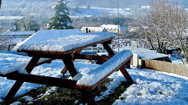 Ein mit Schnee bedecktes Picknicktisch mit freiem Blick auf ein Bergmassiv im Hintergrund.