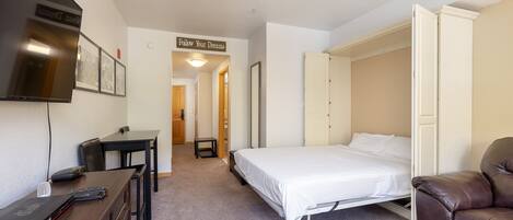 A bedroom with a bed, a desk with a laptop, a TV, and a brown leather chair.