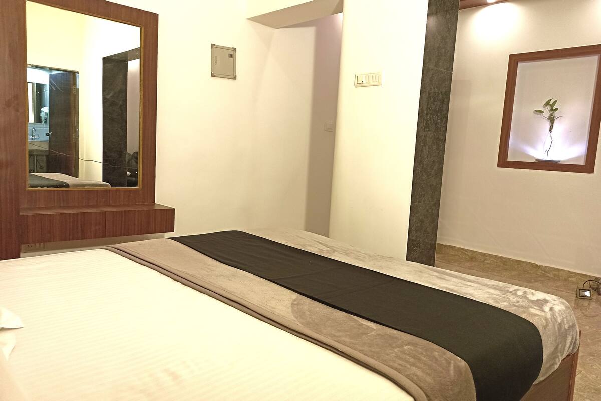 Habitación de hotel con cama, un espejo grande, una lámpara de pared y un cuadro enmarcado.
