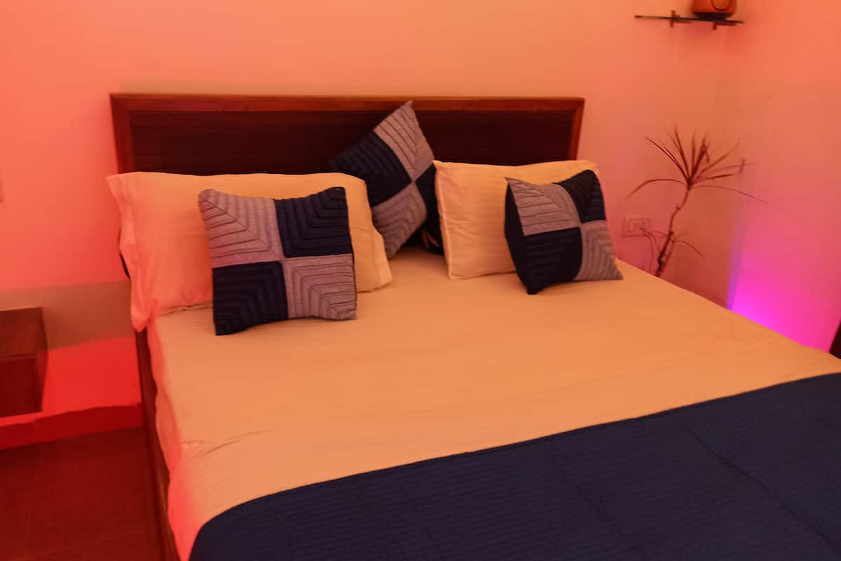 Una cama con cabecera de madera, varios almohadones y una mesita de noche.