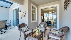 Un espace patio aménagé avec des meubles en osier, une table en verre et une vue sur l’intérieur grâce à des portes vitrées.