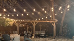 An outdoor patio with string lights, wooden chairs, and a covered seating area. - Coastal Boho Beach Escape - 1 block to paradise (Jacksonville Beach)