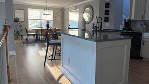 A modern kitchen with a central island, a dining area with a table and chairs, and a view of the outdoors. - Coastal Boho Beach Escape - 1 block to paradise (Jacksonville Beach)
