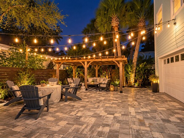 An outdoor patio with a pergola, string lights, and seating arrangements.