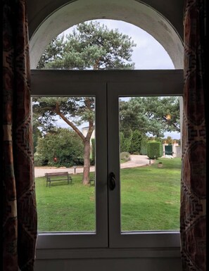 Blick durch eine doppelte Tür mit weißem Rahmen auf einen gepflegten Rasen und einen großen Baum.