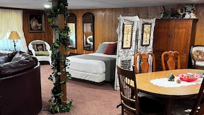 Una sala de estar acogedora con piso de madera, una mesa de comedor con sillas, un sofá, una cama y un espejo grande.