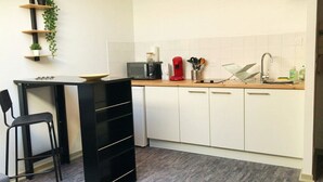 A compact kitchen with a black countertop, white cabinets, and a small dining area with a black chair. - STUDIO LE NID ★ PLEIN CENTER ★ LUMINEUX ★ WIFI (Valence d'Agen)