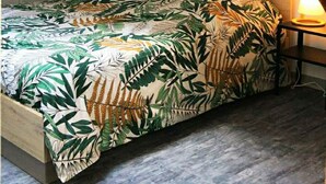 A bedroom with a sloped ceiling, a bed with a tropical leaf pattern bedspread, a bedside table with a lamp, and a wooden beam structure. - STUDIO LE NID ★ PLEIN CENTER ★ LUMINEUX ★ WIFI (Valence d'Agen)