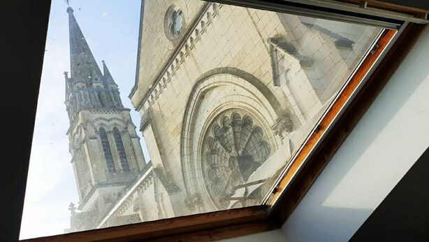 A skylight with a view of a church's facade, including a pointed spire and an arched window. - STUDIO LE NID ★ PLEIN CENTER ★ LUMINEUX ★ WIFI (Valence d'Agen)