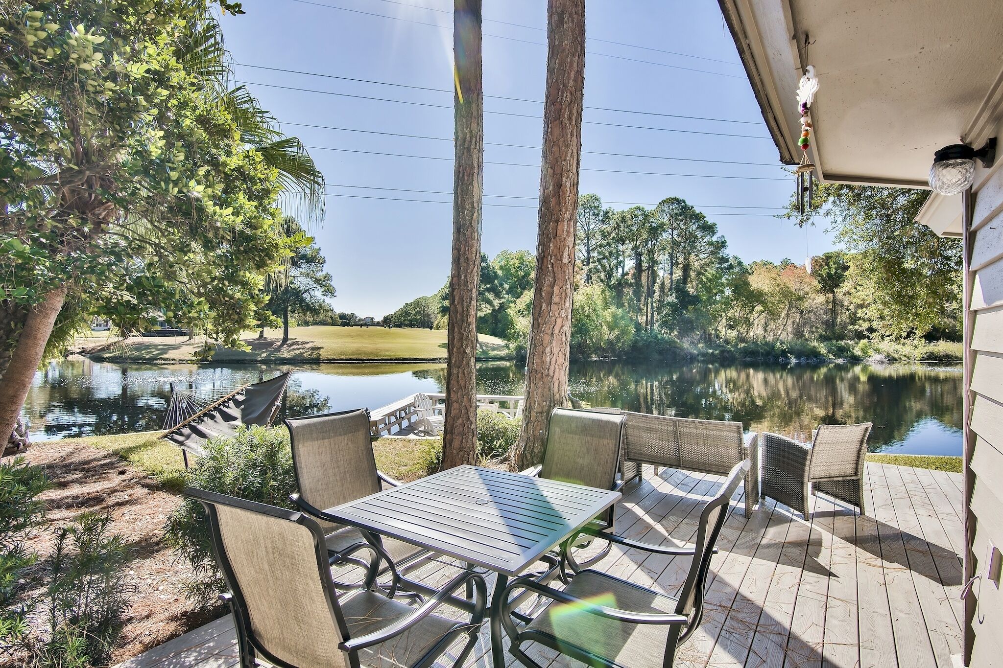 Une terrasse avec une table et des chaises donnant sur un étang et des arbres.