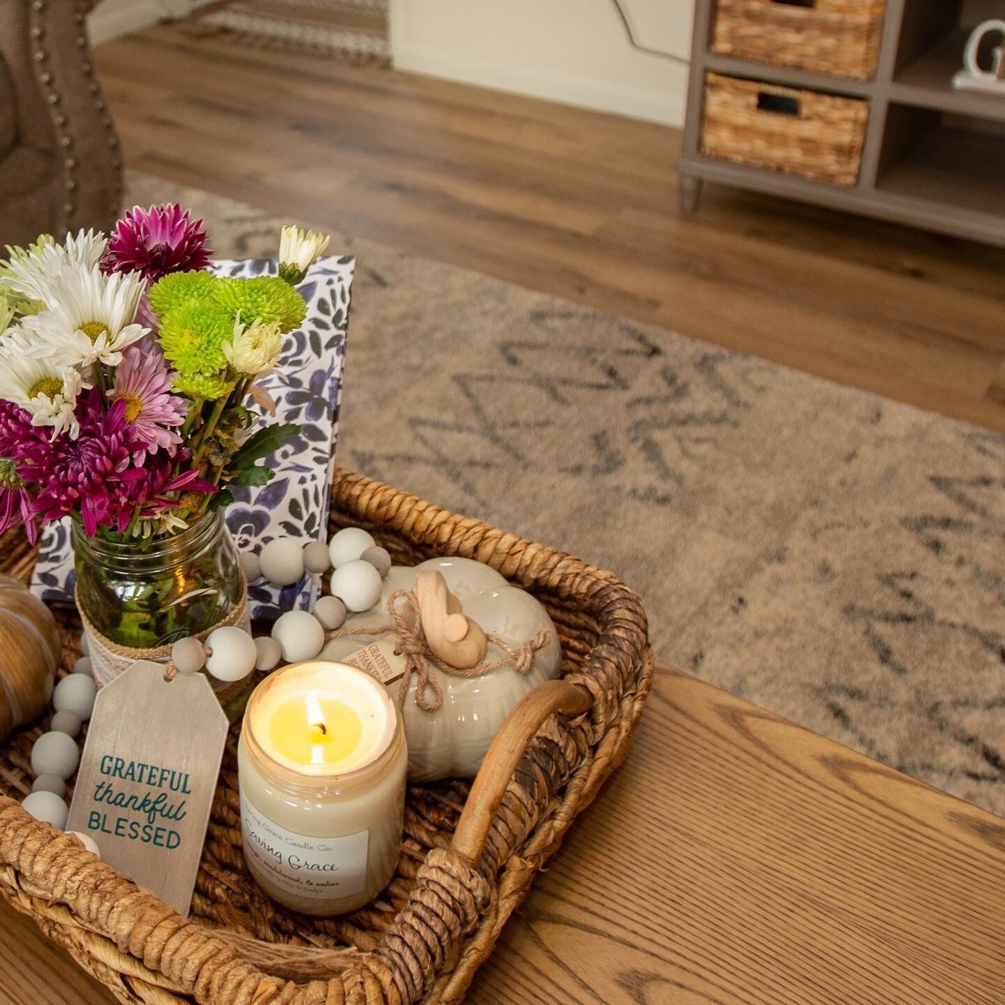 A wicker tray with a candle, a jar of flowers, and a candle label.