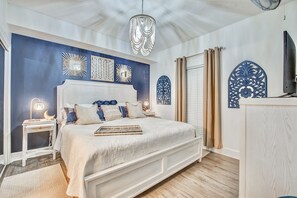 A bedroom with a large bed, a nightstand, a lamp, decorative wall art, and a television. - Beachfront~King Bed~Beach Chairs~5 pools (Panama City Beach)