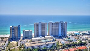 A coastal hotel complex with multiple high-rise buildings, a parking area, and a beach in the background.