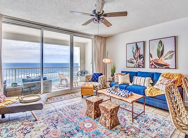 A spacious living room with a large balcony, a ceiling fan, and a view of the ocean. - Beachfront~King Bed~Beach Chairs~5 pools (Panama City Beach)