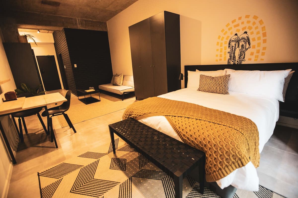 A modern hotel room with a bed, a desk, a chair, a bench, and a wall with a circular design.