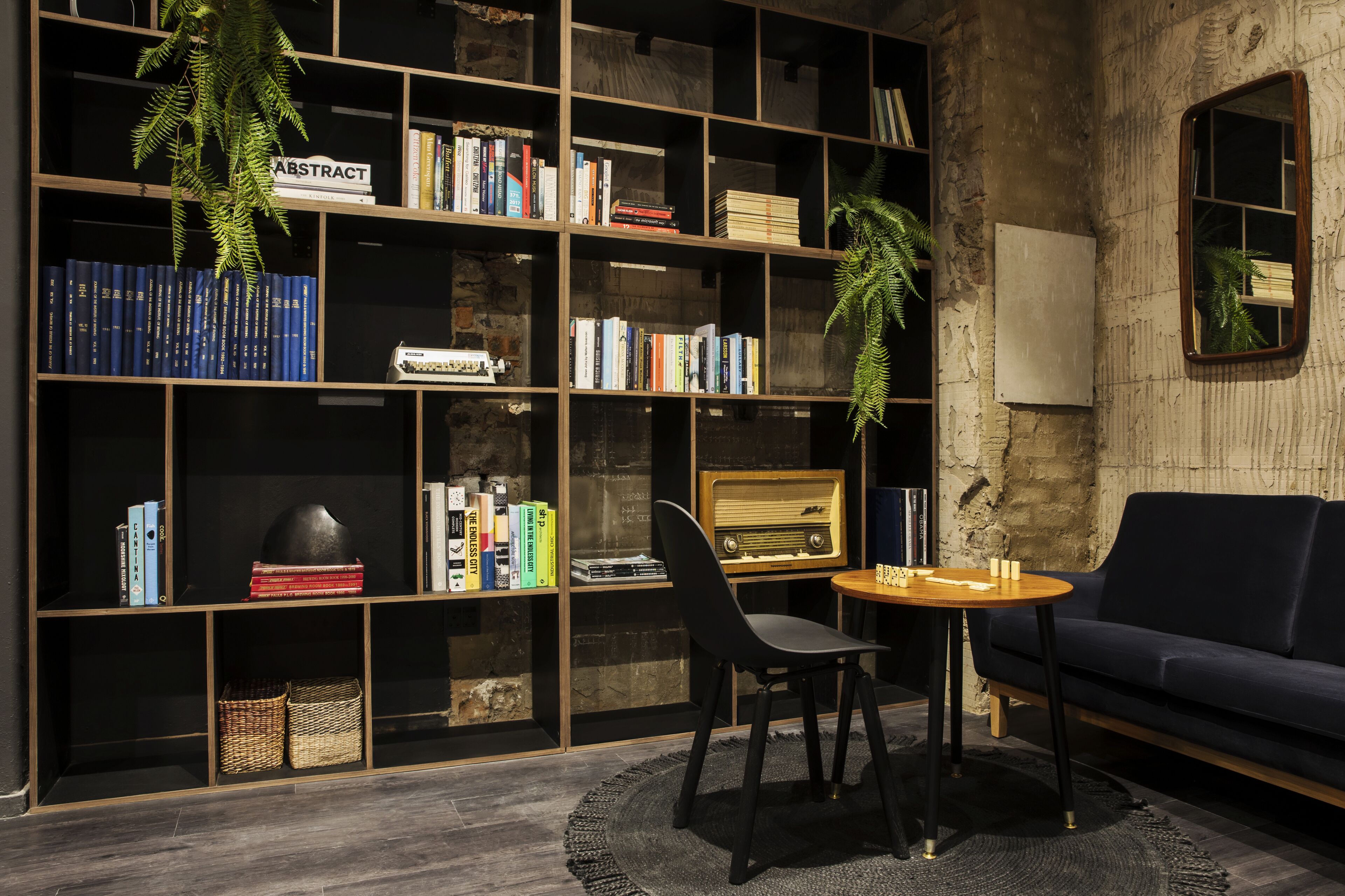 A room with a large bookshelf, a vintage radio, a dark sofa, and a round table with chairs.
