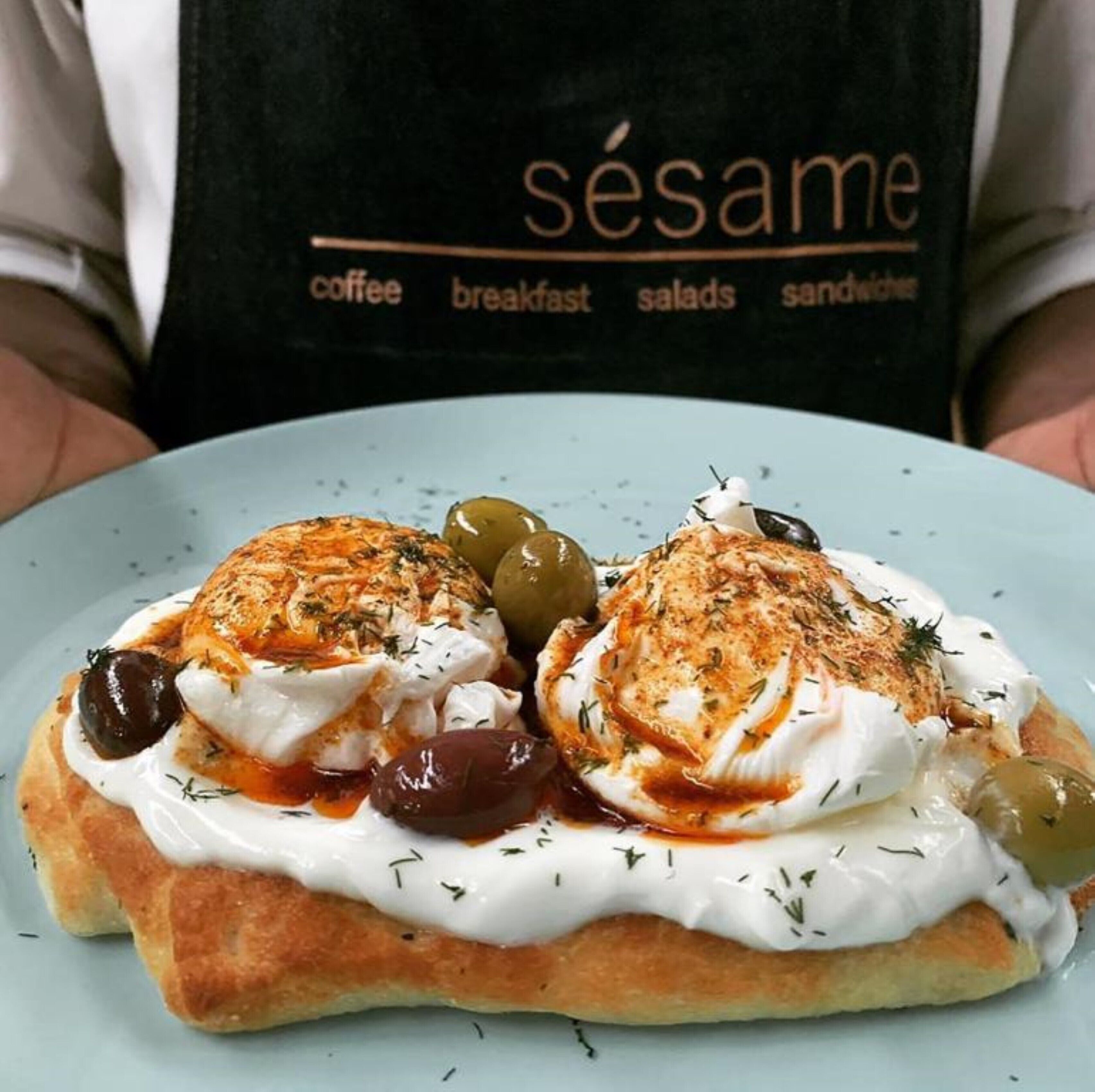 Un plato de comida con dos huevos pochados cubiertos de salsa y aceitunas, servido sobre una rebanada de pan.