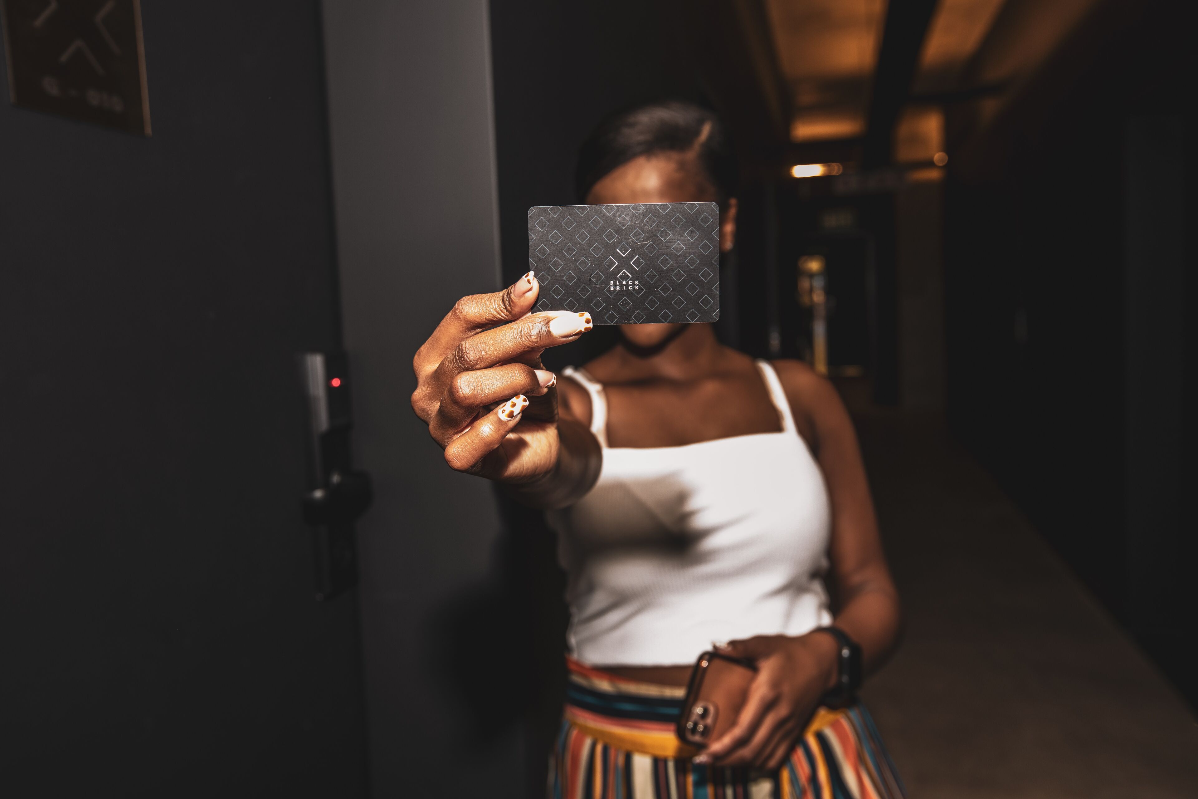 A person holding a card in a dimly lit hallway with a door and a light switch visible.