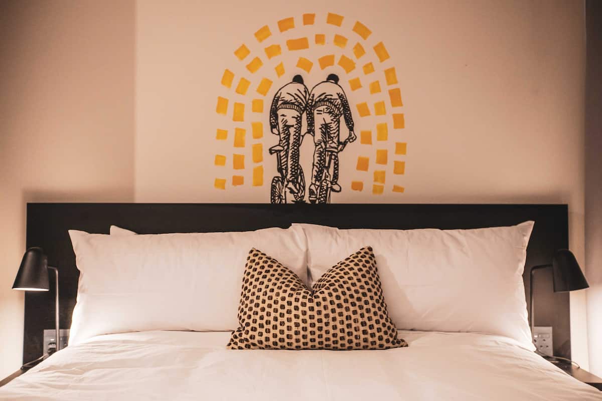 A hotel room with a bed, pillows, a headboard, and a wall decoration.